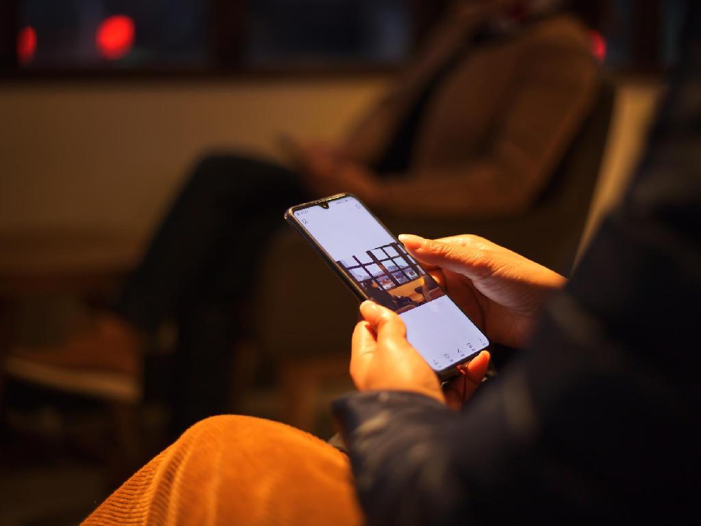 شخصی در حال کار با گوشی هوشمند جدید در فضای داخلی با نور گرم