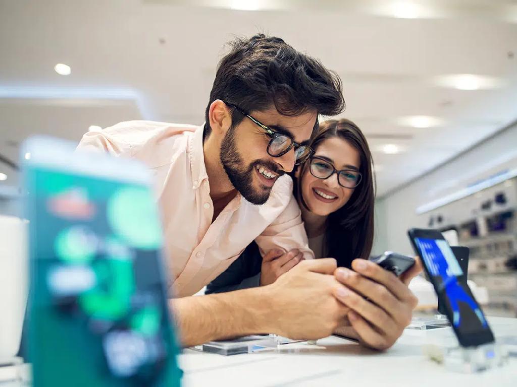 زوج جوان در حال بررسی گوشی موبایل در فروشگاه برای خرید اقساطی
